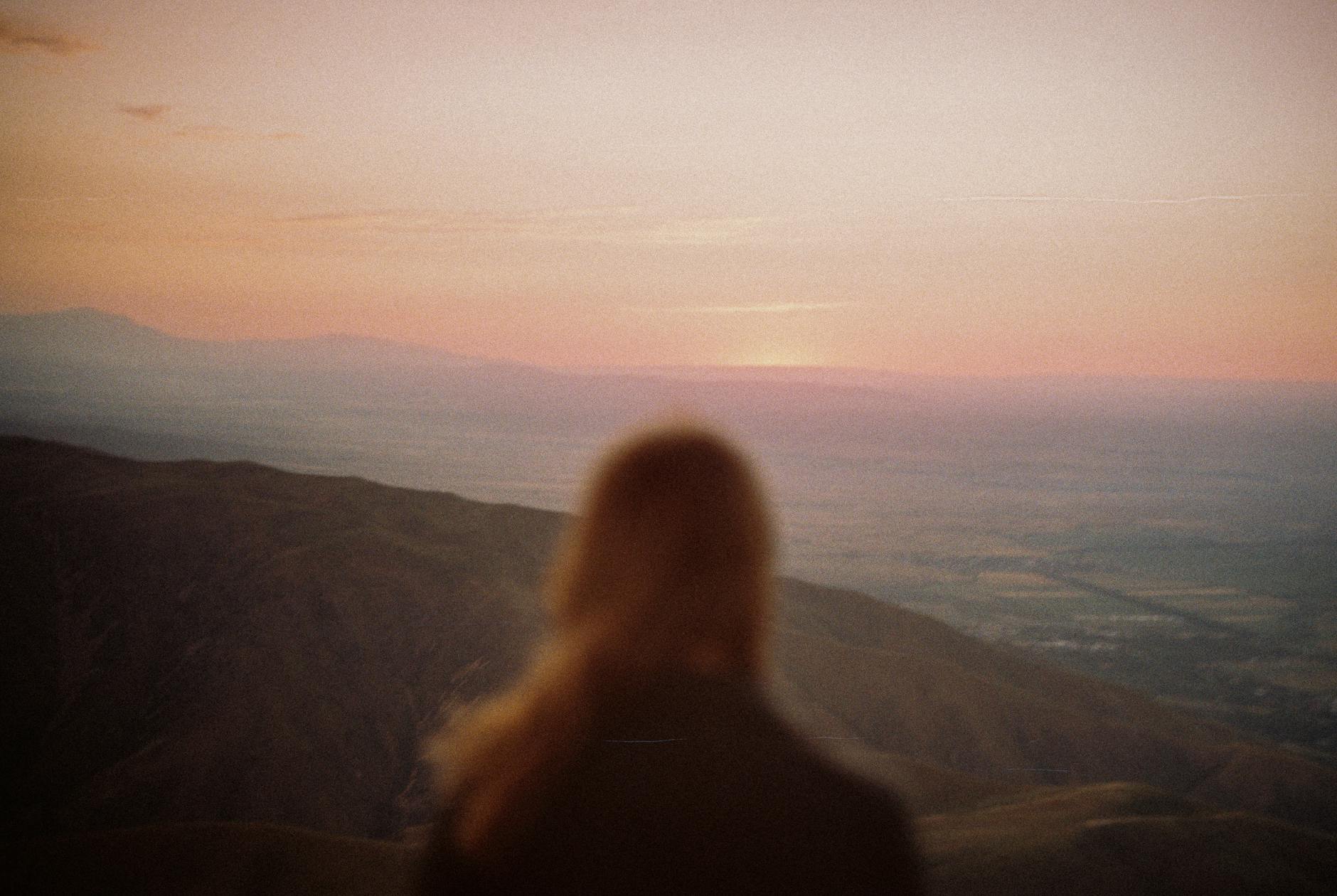 Blurred silhouette of a woman looking out over mountains at sunset, symbolizing the feeling of being invisible or unseen.